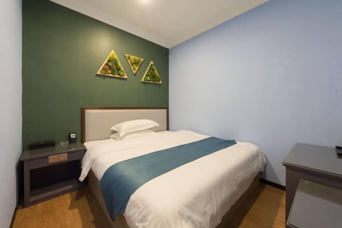 A hotel room with a bed, bedside table, and a wall-mounted artwork.