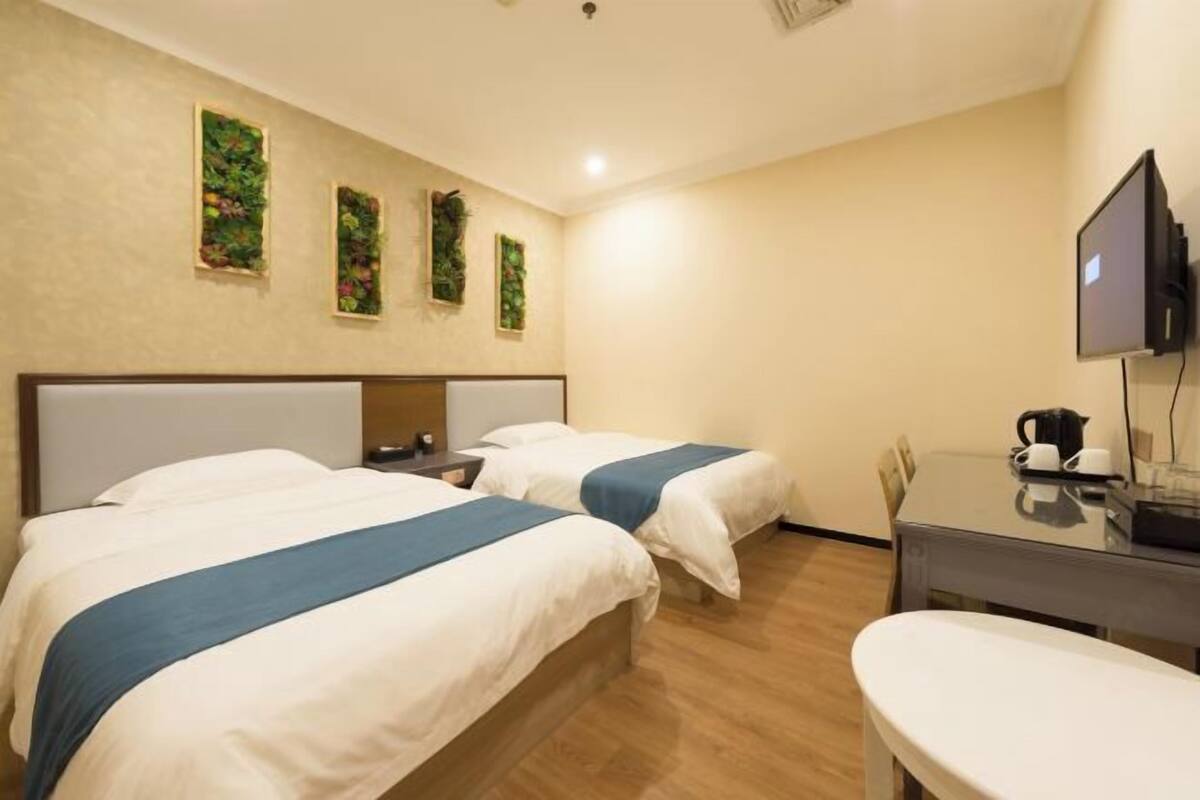 A hotel room with two beds, a desk, a chair, a television, and wall-mounted artwork.