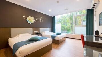 Een hotelkamer met twee bedden, een bureau en uitzicht op groen.