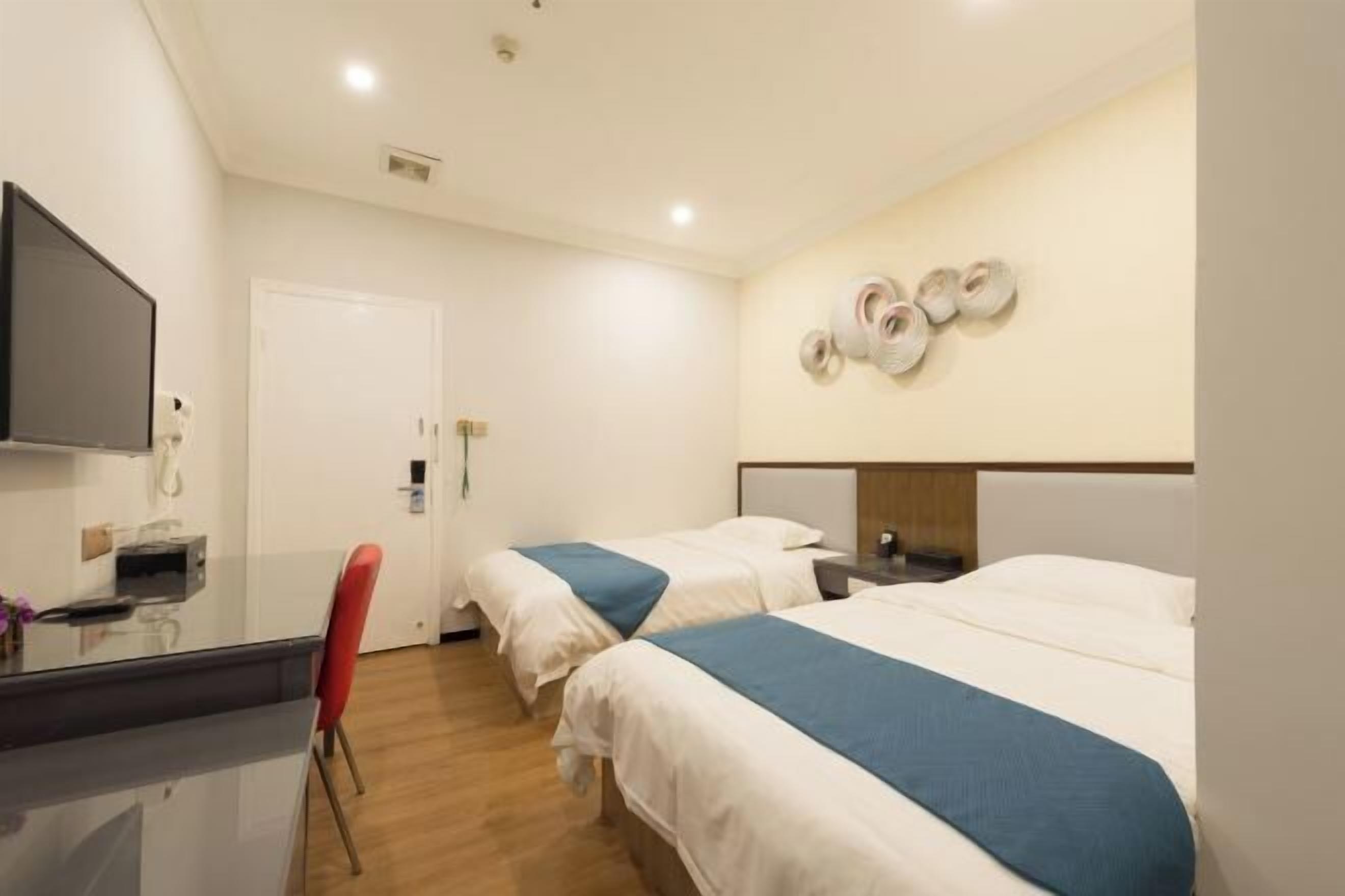 Habitación de hotel con dos camas, un escritorio con silla, televisión y un zapatero en la pared.