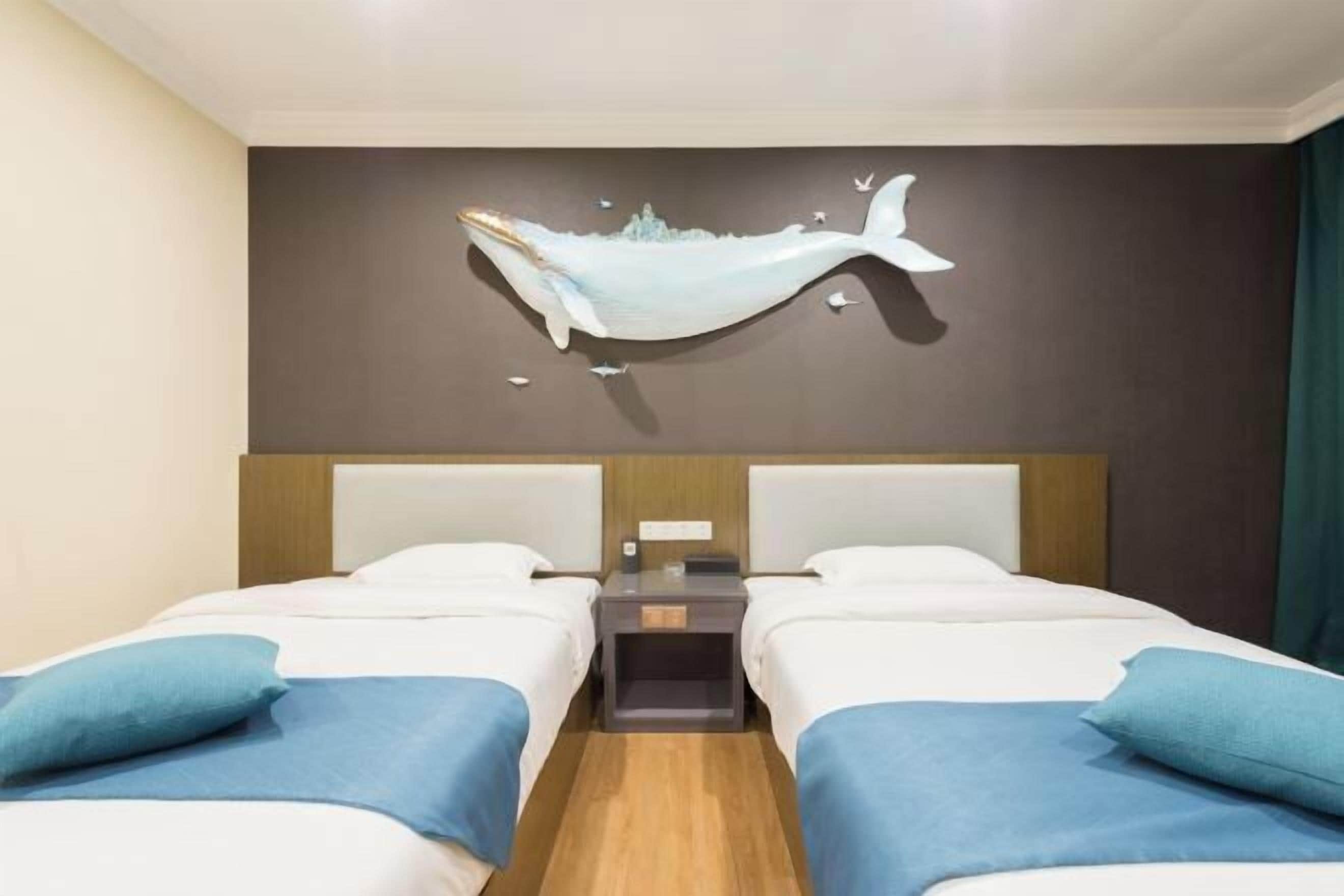 Een hotelkamer met twee bedden, een nachtkastje, een kunstwerk van een walvis aan de muur, en een houten vloer.