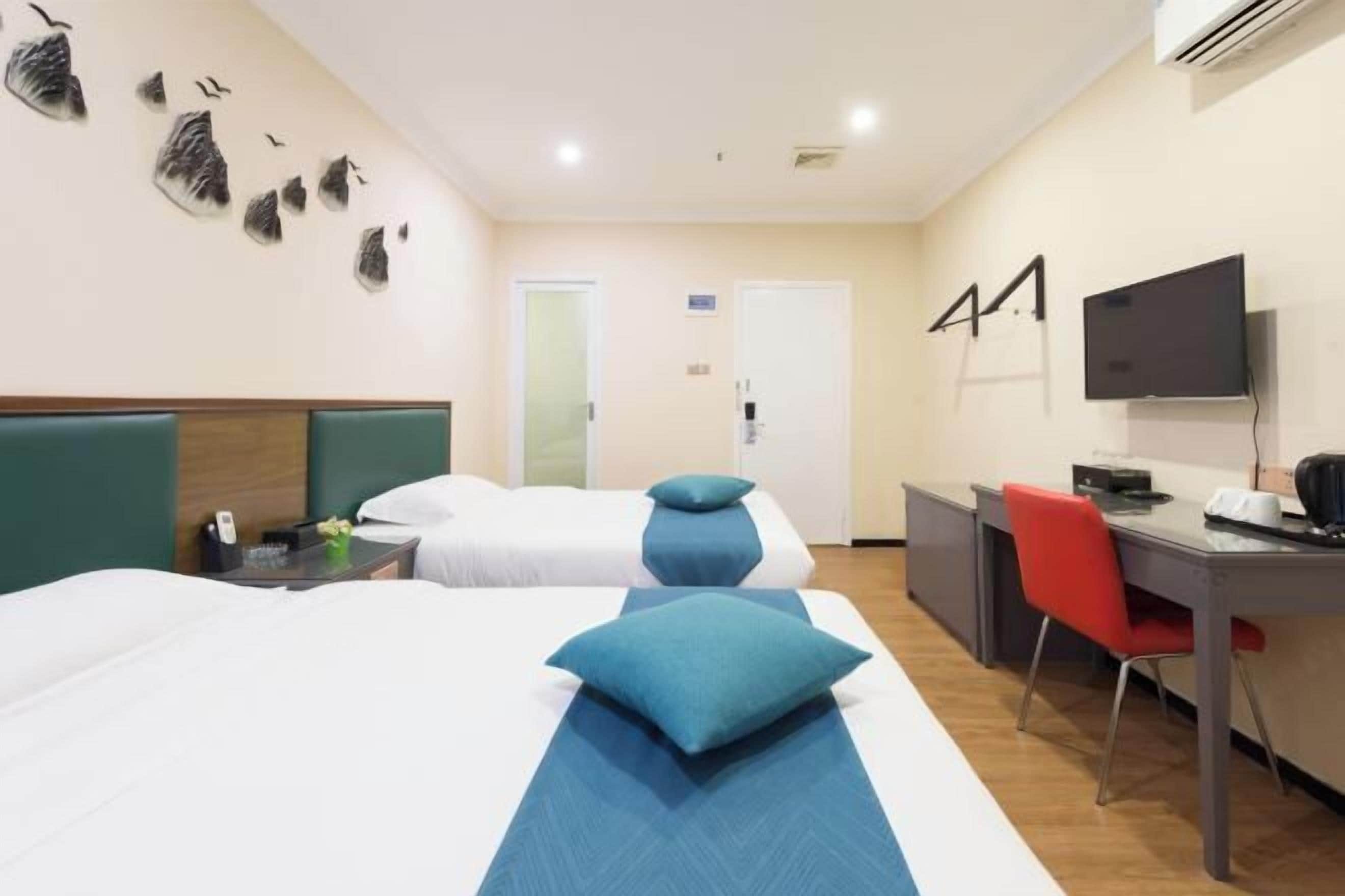 Habitación de hotel con dos camas, un escritorio, una silla, un televisor y una obra de arte colgada en la pared.