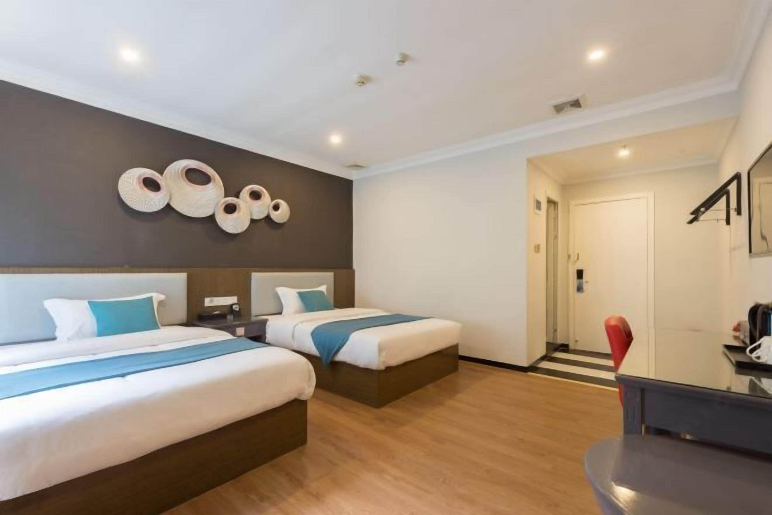 Een hotelkamer met twee bedden, een houten vloer, een kunstwerk aan de muur en een deur naar een andere kamer.