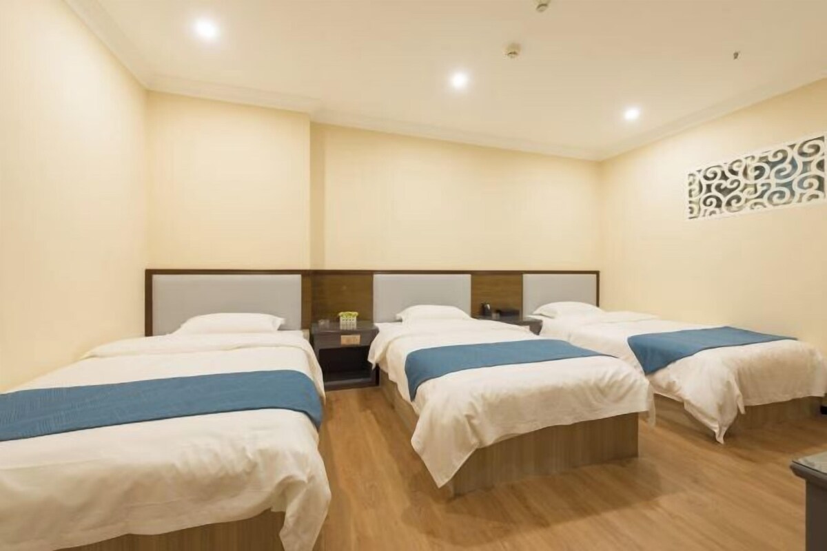 Habitación de hotel con cuatro camas individuales en fila, suelo de madera y un panel decorativo en la pared.