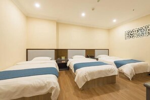 Habitación de hotel con cuatro camas individuales en fila, suelo de madera y un panel decorativo en la pared.