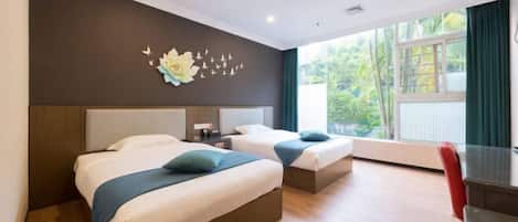 Une chambre d’hôtel avec deux lits, un bureau, une chaise et une vue sur la verdure environnante.