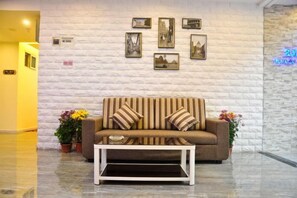 A lobby with a sofa and coffee table, a white brick wall, and framed pictures. - Guangzhou Huiyin Fashion Hotel (Pazhou Convention and Exhibition Xingang East Subway Station) (Guangzhou)