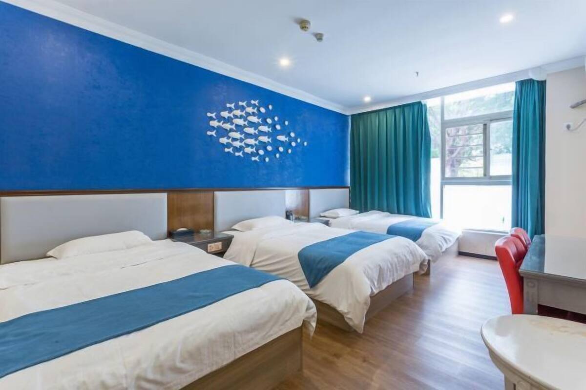 A hotel room with three beds, a large window with curtains, and a wall mural of fish.