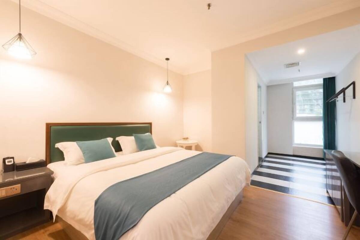 A modern hotel room with a large bed, a bedside table, a lamp, and a view of the hallway.