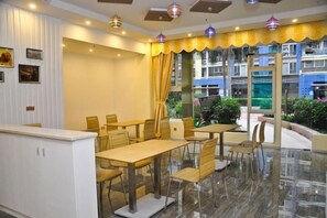 A hotel dining area with tables and chairs, a reception desk, and a view of the building's exterior. - Guangzhou Huiyin Fashion Hotel (Pazhou Convention and Exhibition Xingang East Subway Station) (Guangzhou)