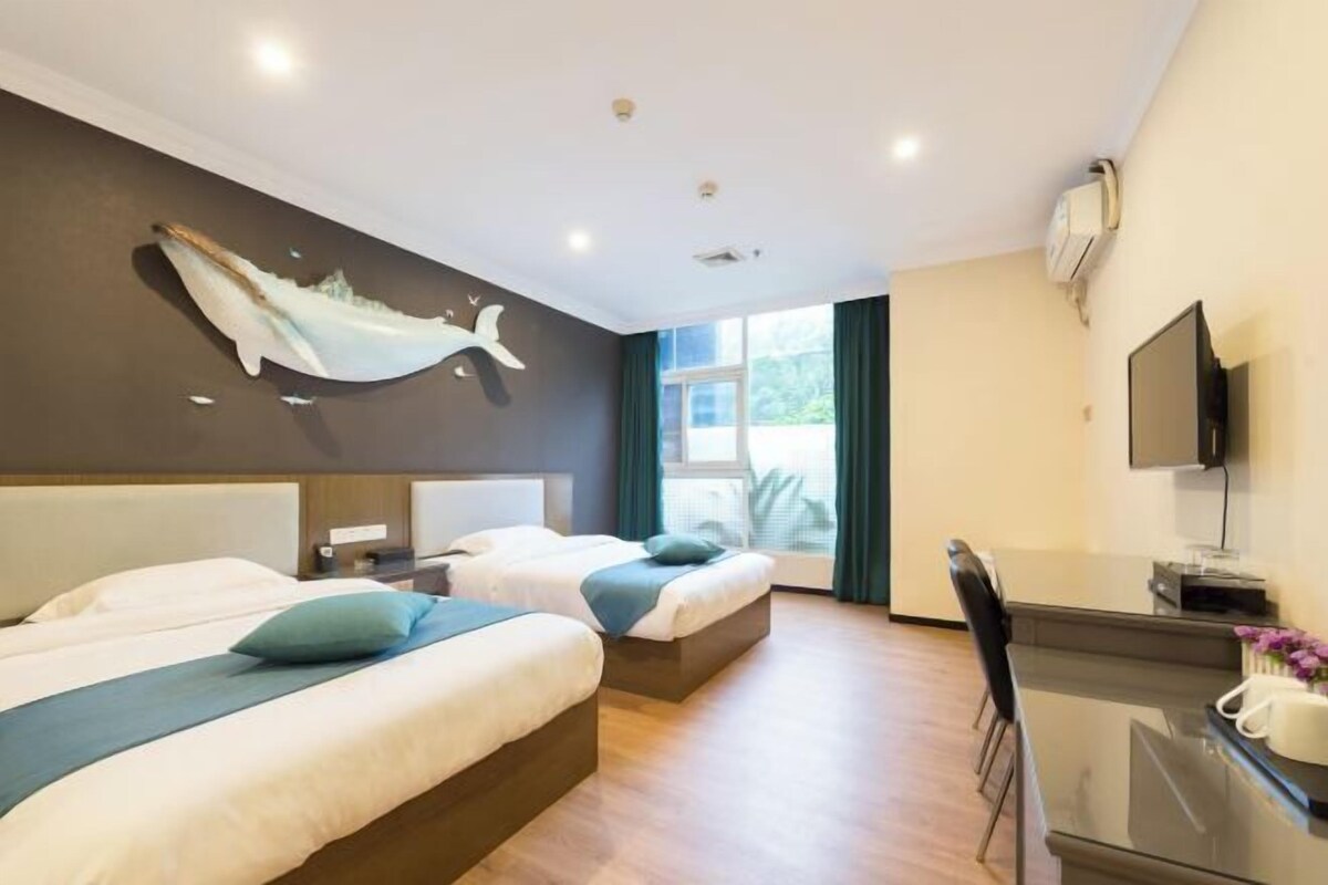 Habitación de hotel con dos camas, un escritorio, un televisor y un ventanal grande.