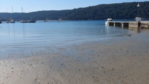 A sandy beach with boats docked in the background and a pier extending into the water. - Apartment Marta (Rab)