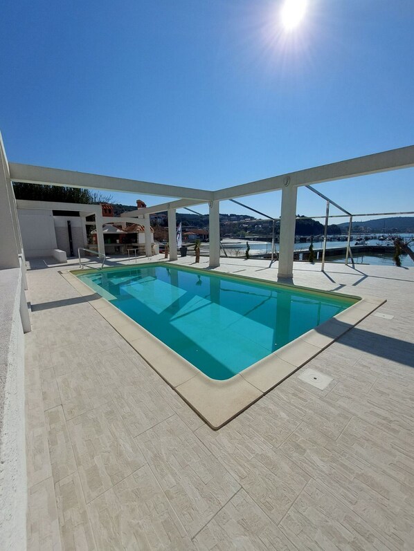 A rectangular swimming pool with a clear blue water surface, surrounded by a light-colored tiled deck.