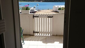 A view from a room's door to a balcony with a white railing, a tiled floor, and a clear view of a lake and boats. - Apartment Marta (Rab)