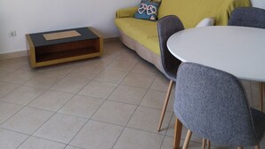 A modern living room with a yellow sofa, a small table, and a grey chair. There is a wall-mounted shelf with a painting and a wooden cabinet. - Apartment Marta (Rab)