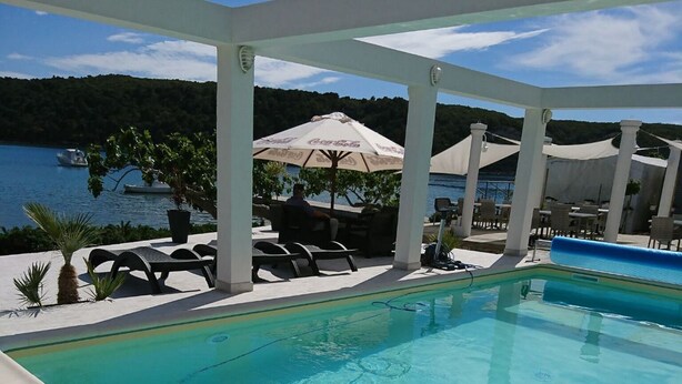 A swimming pool with a view of the sea, lounge chairs, and umbrellas. - Apartment Marta (Rab)
