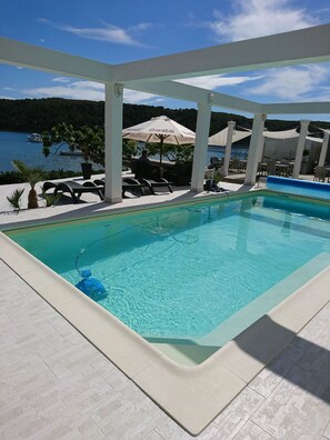 A swimming pool with a view of the sea, lounge chairs, and umbrellas. - Apartment Marta (Rab)