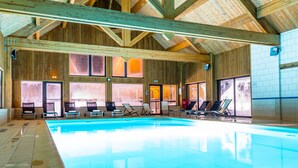 Una piscina interior amplia con vigas de madera y múltiples tumbonas.