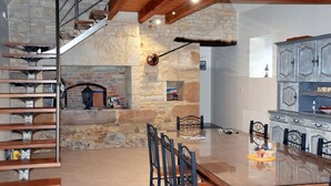 A dining area with a glass table and chairs, a stone fireplace, and a staircase with metal railings.