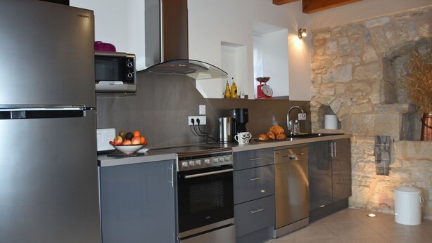 A modern kitchen with stainless steel appliances, a stone wall, and a wooden ceiling.