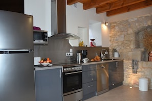 A modern kitchen with stainless steel appliances, a stone wall, and a wooden ceiling.
