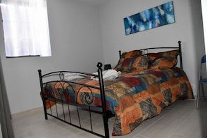 A single bed with a metal frame, a colorful quilt, and a blue abstract painting on the wall.