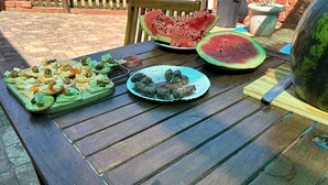 A wooden table with food items including a watermelon slice, a plate of meatballs, and a tray of appetizers. - 6 Sleeper self catering house (L'Agulhas)