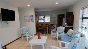 A living room with a white sofa, striped armchairs, a coffee table, and a TV mounted on the wall. - 6 Sleeper self catering house (L'Agulhas)