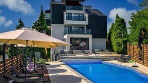 Un edificio moderno de dos pisos con piscina, mobiliario exterior y una silla colgante.