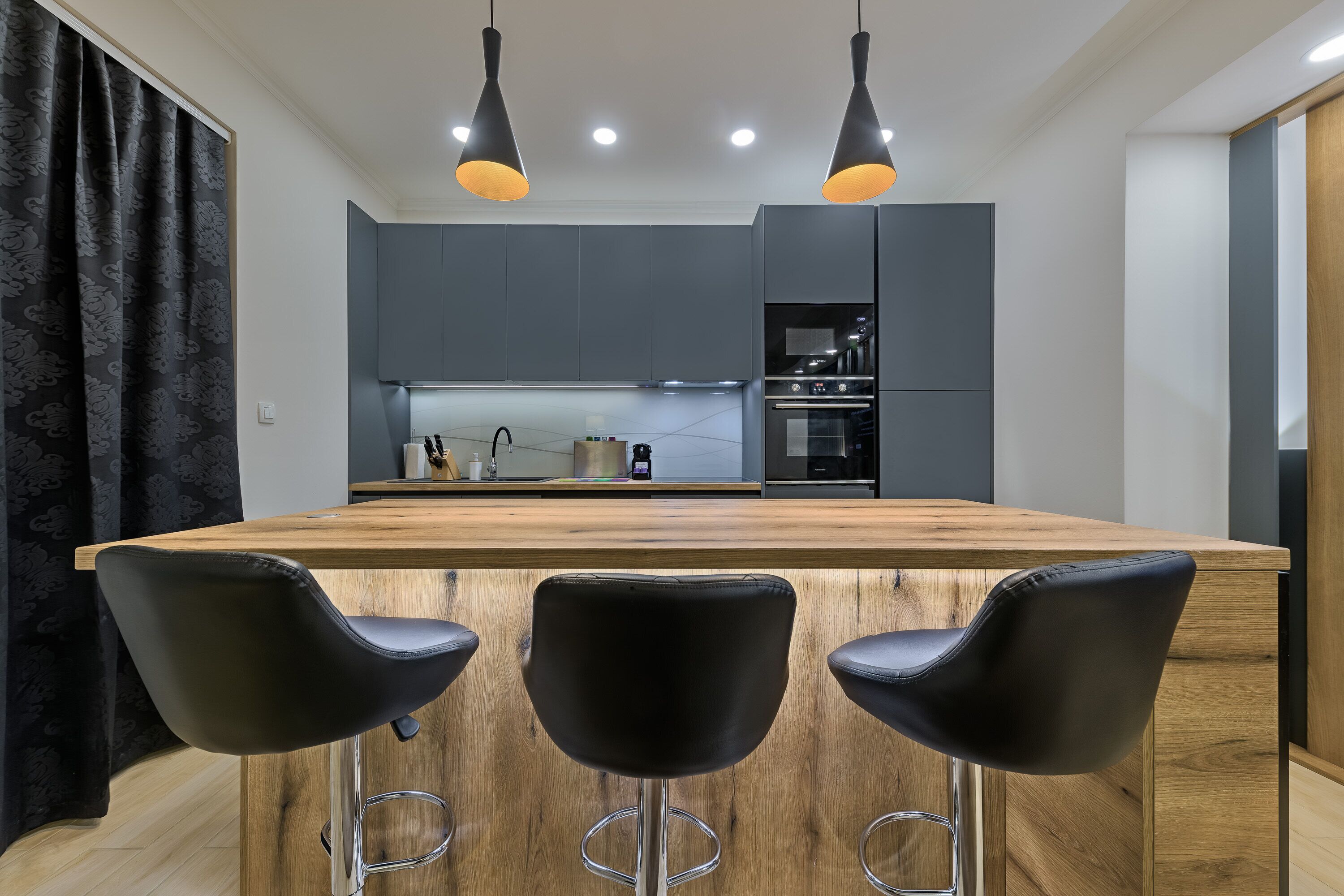 A modern kitchen with a wooden island and black bar stools.