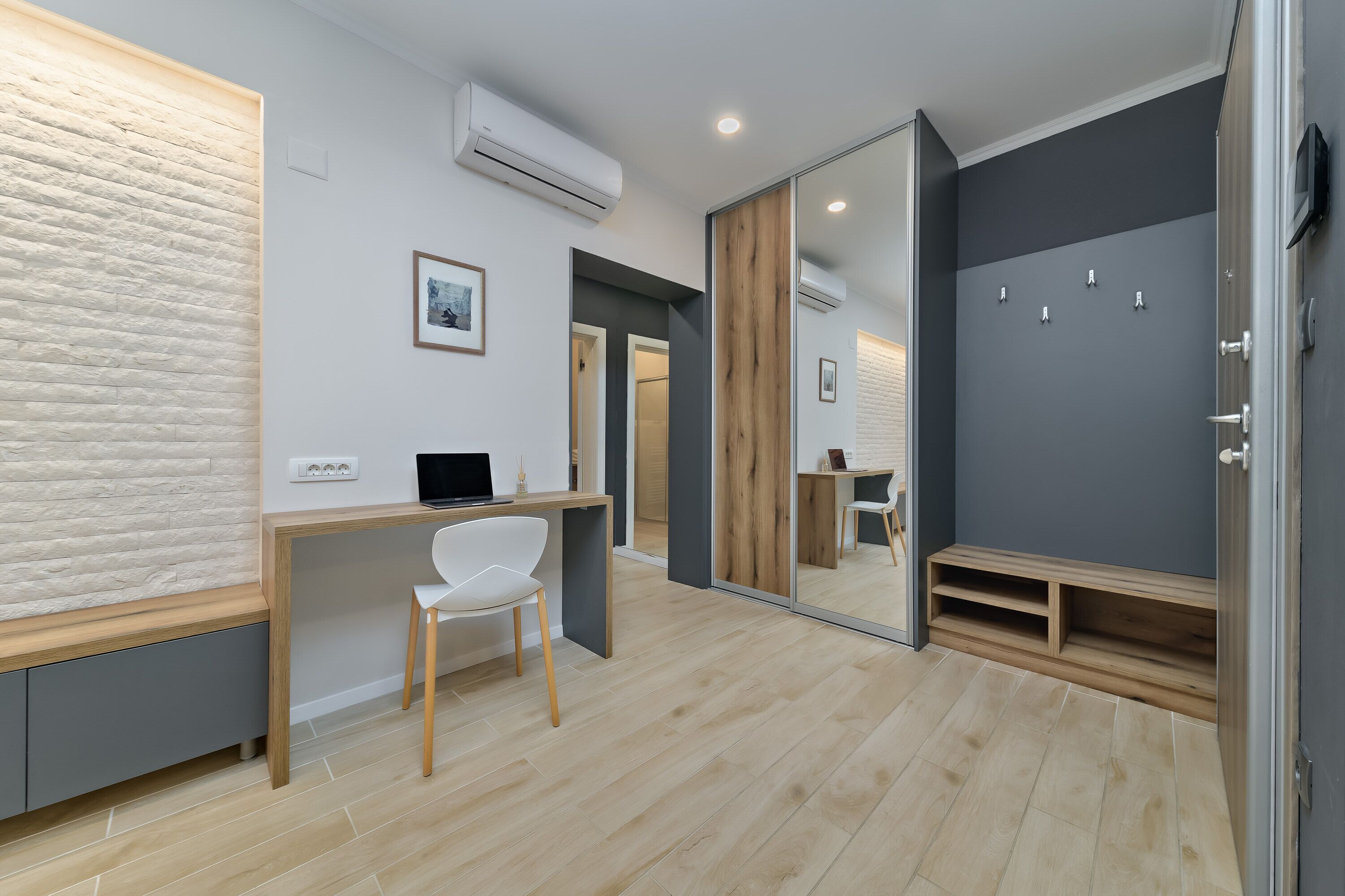 A modern room with a wooden desk, a white chair, a mirror, and a built-in bench.