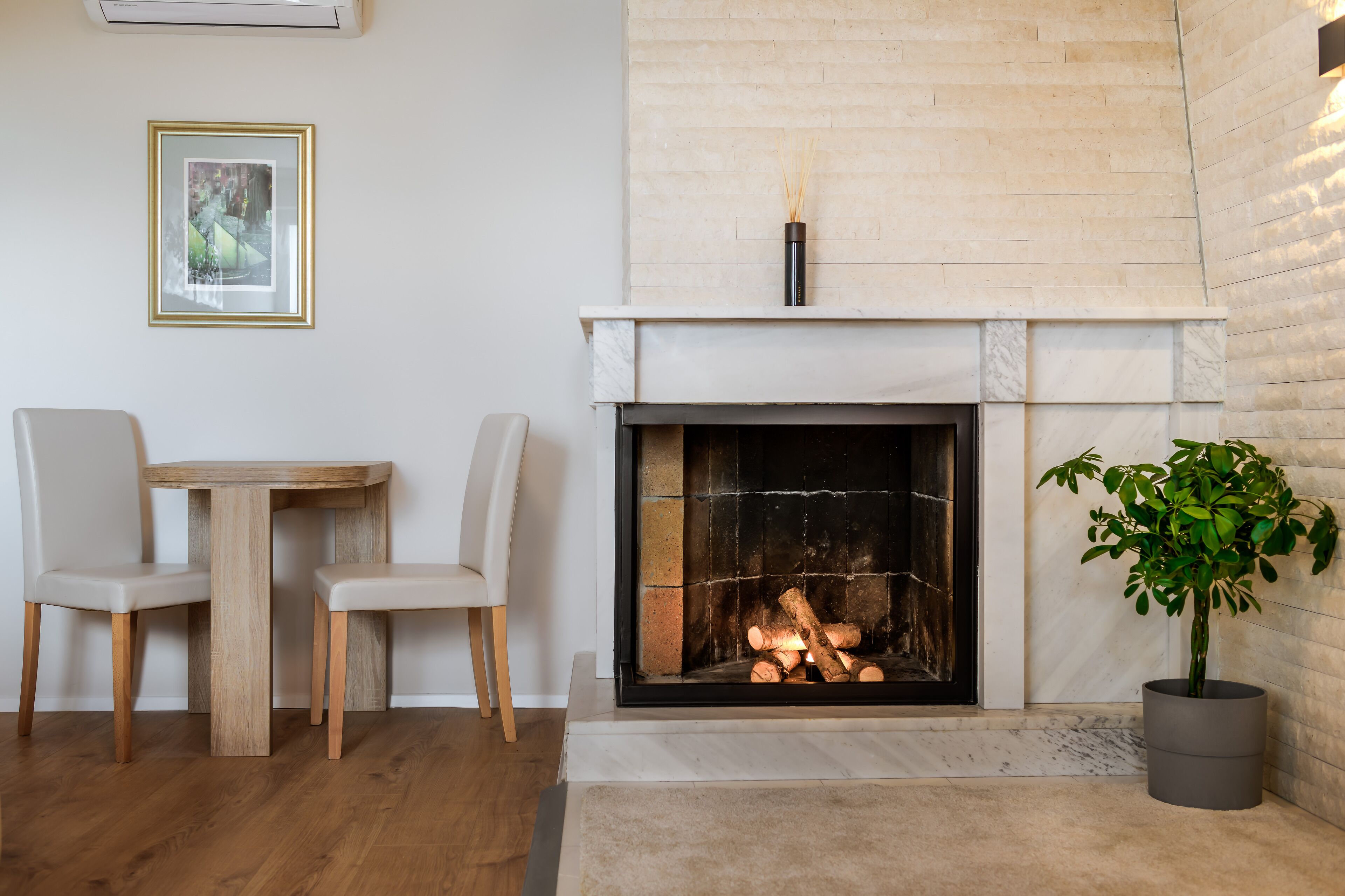A fireplace with logs, a dining table with chairs, and a potted plant.