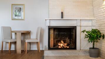 A fireplace with logs, a dining table with chairs, and a potted plant.