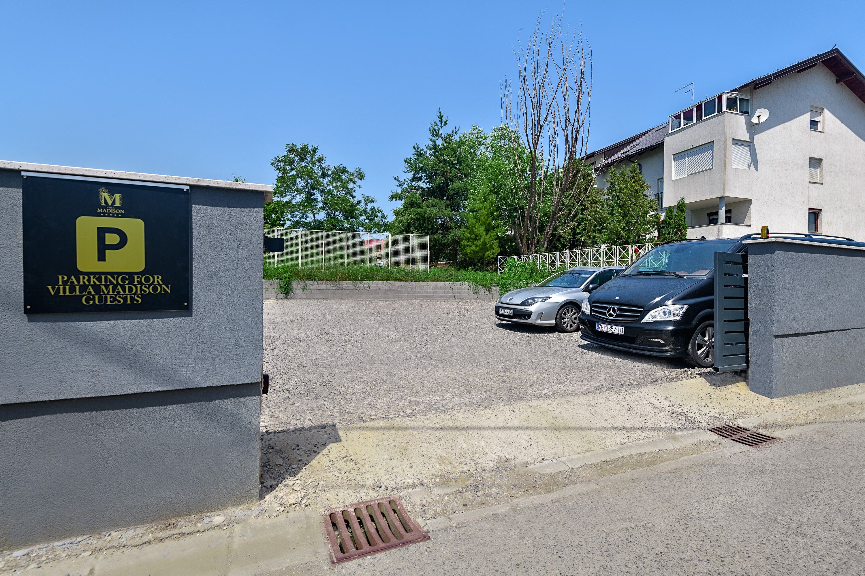 Ein Parkplatz mit Schild für Villa Madison-Gäste, mit Kiesbefestigung und einem Gebäude mit befestigtem Eingang.