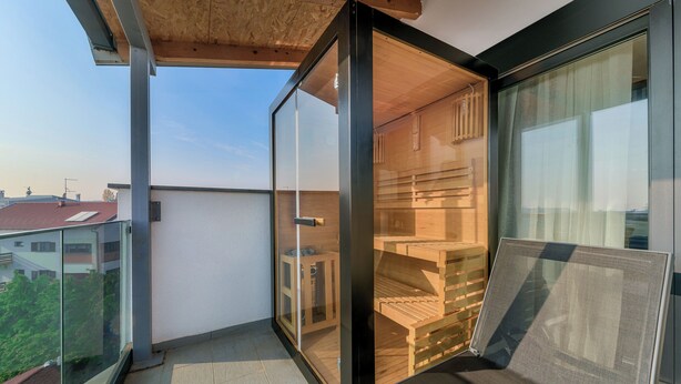 Un balcón con puerta de cristal que da a un interior de madera, vista de la ciudad y cielo despejado.