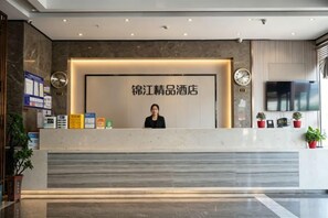 A hotel reception desk with a large sign, a clock, and a TV screen. - Xinjinjiang Boutique Hotel (Dai County)