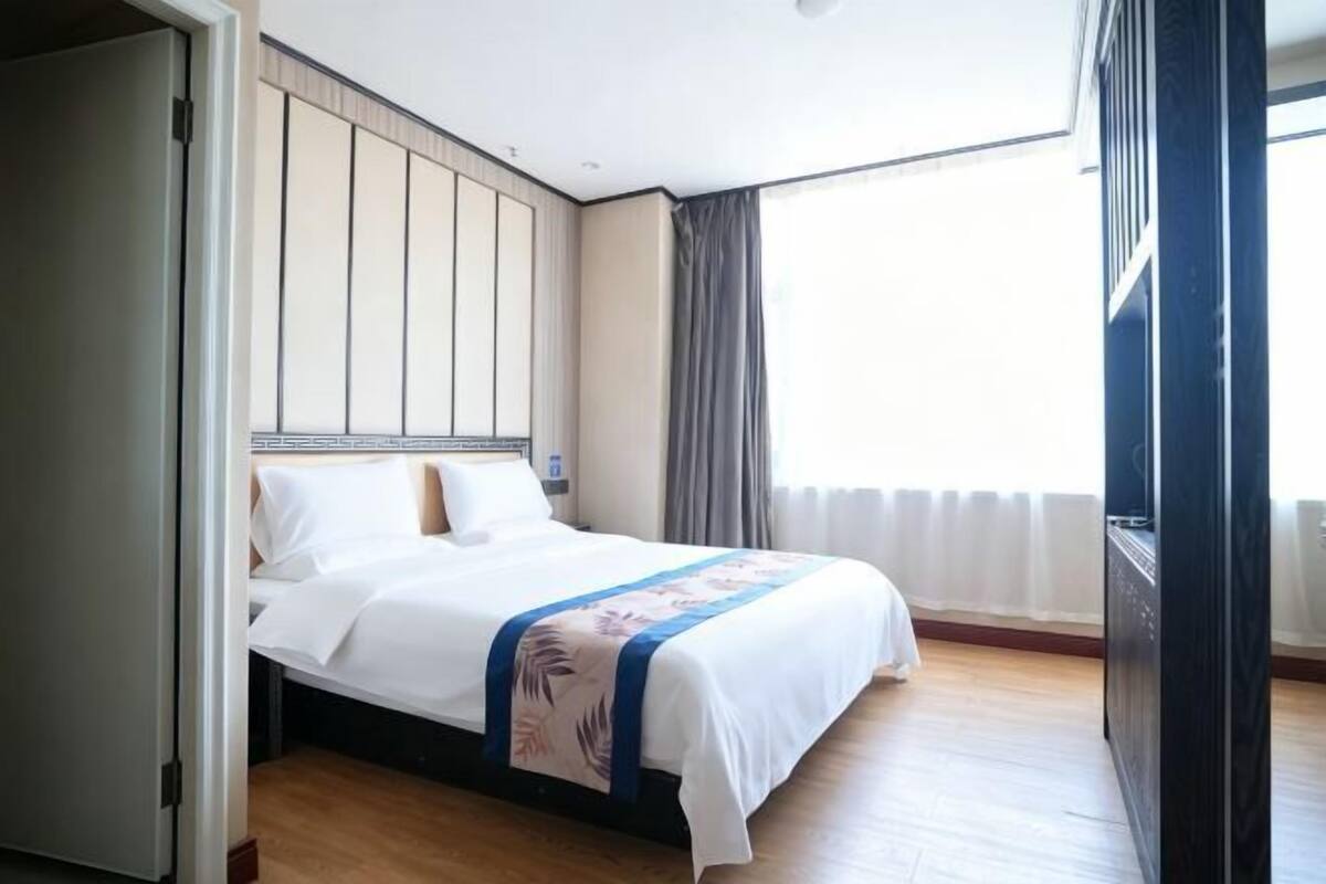 A hotel room with a bed, a wardrobe, a television, and a window with curtains.