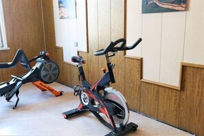 Two stationary bikes in a room with wooden paneling and a painting on the wall. - Xinjinjiang Boutique Hotel (Dai County)