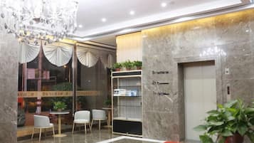 A hotel lobby with a chandelier, a reception desk, a seating area, and an elevator.