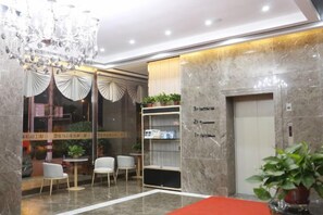 Un vestíbulo de hotel con candelabro, una recepción, una zona de estar y un ascensor.