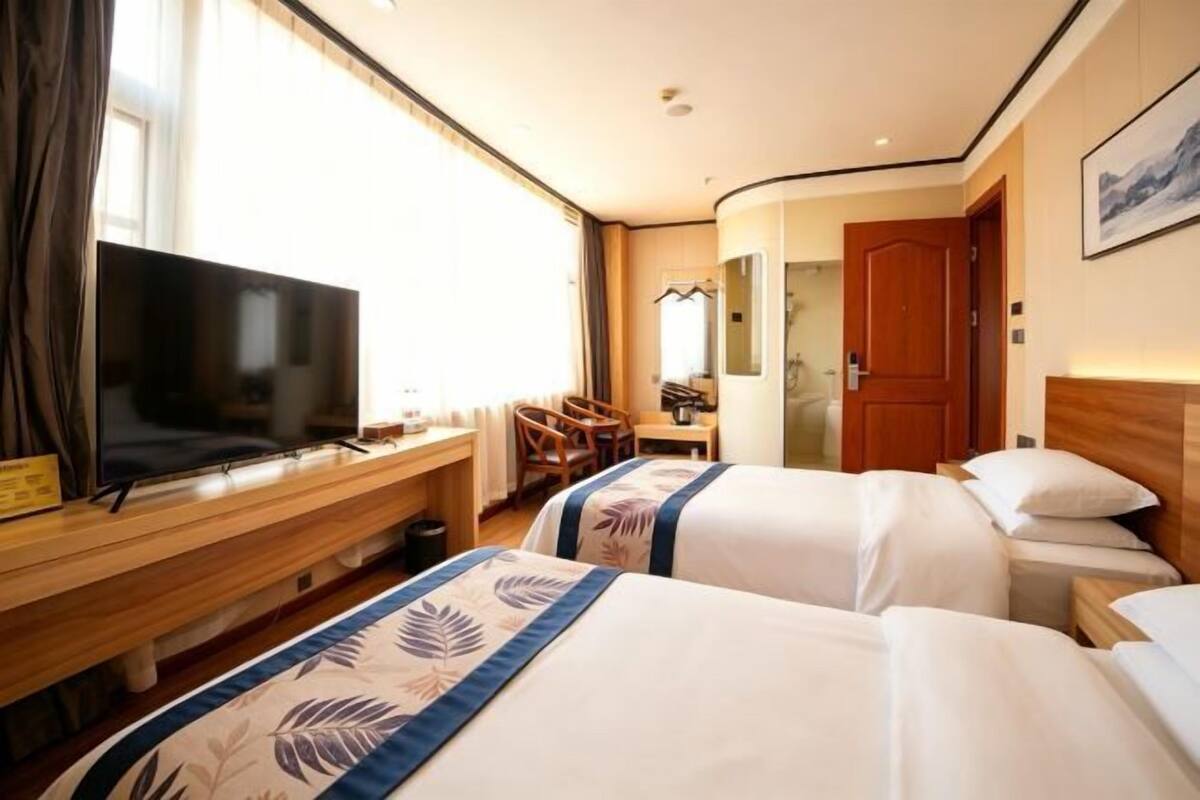 A hotel room with two beds, a TV, a desk, and a shower area.