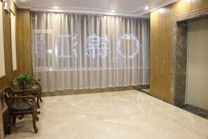Una habitación con un ventanal cubierto por cortinas traslúcidas, una silla de madera y un suelo de mármol.