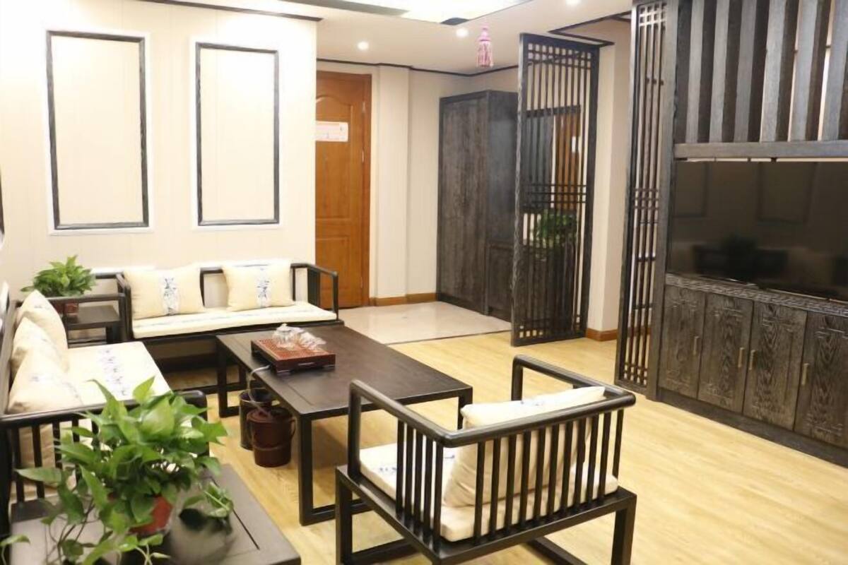 A modern living room with a sofa, coffee table, and chairs. There is a TV on a cabinet, and a wooden door with a screen.