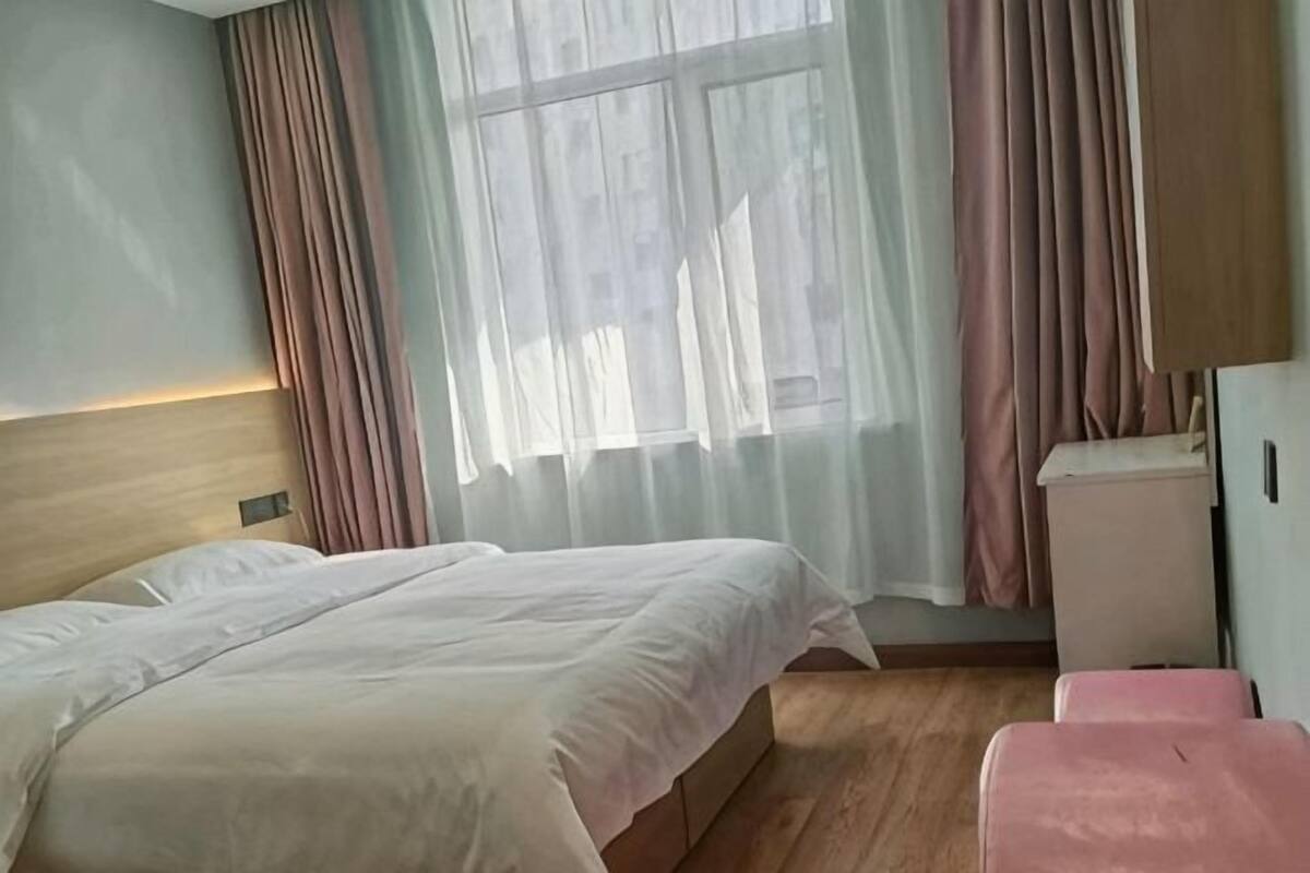 A hotel room with a bed, a bedside table, a small cabinet, and a window with curtains.