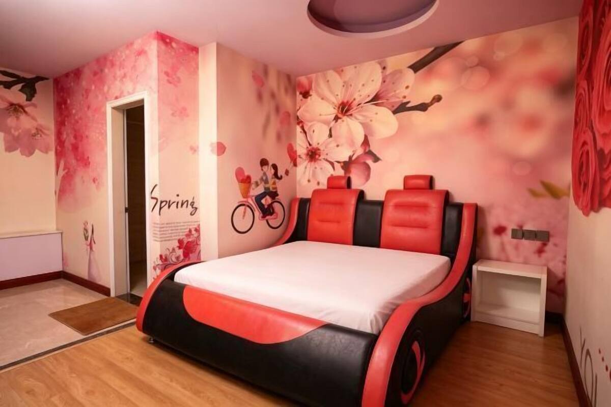 A bedroom with a bed, a wall mural, a bicycle, and a small white shelf.