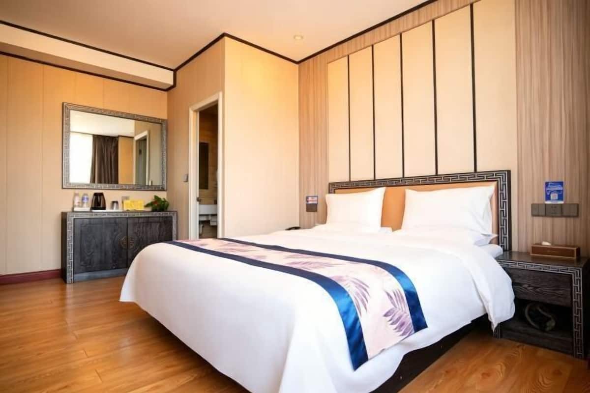 A hotel room with a large bed, a wooden dresser, a mirror, and a nightstand.