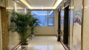 A hotel lobby with a tiled floor, potted plants, a large window, and a wall with a decorative pattern. - Guoken Hotel (Cenxi)