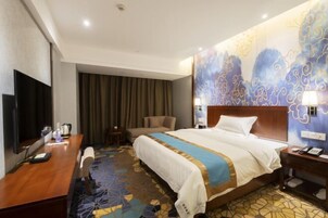Habitación de hotel con cama, escritorio, silla, televisor y alfombra estampada.