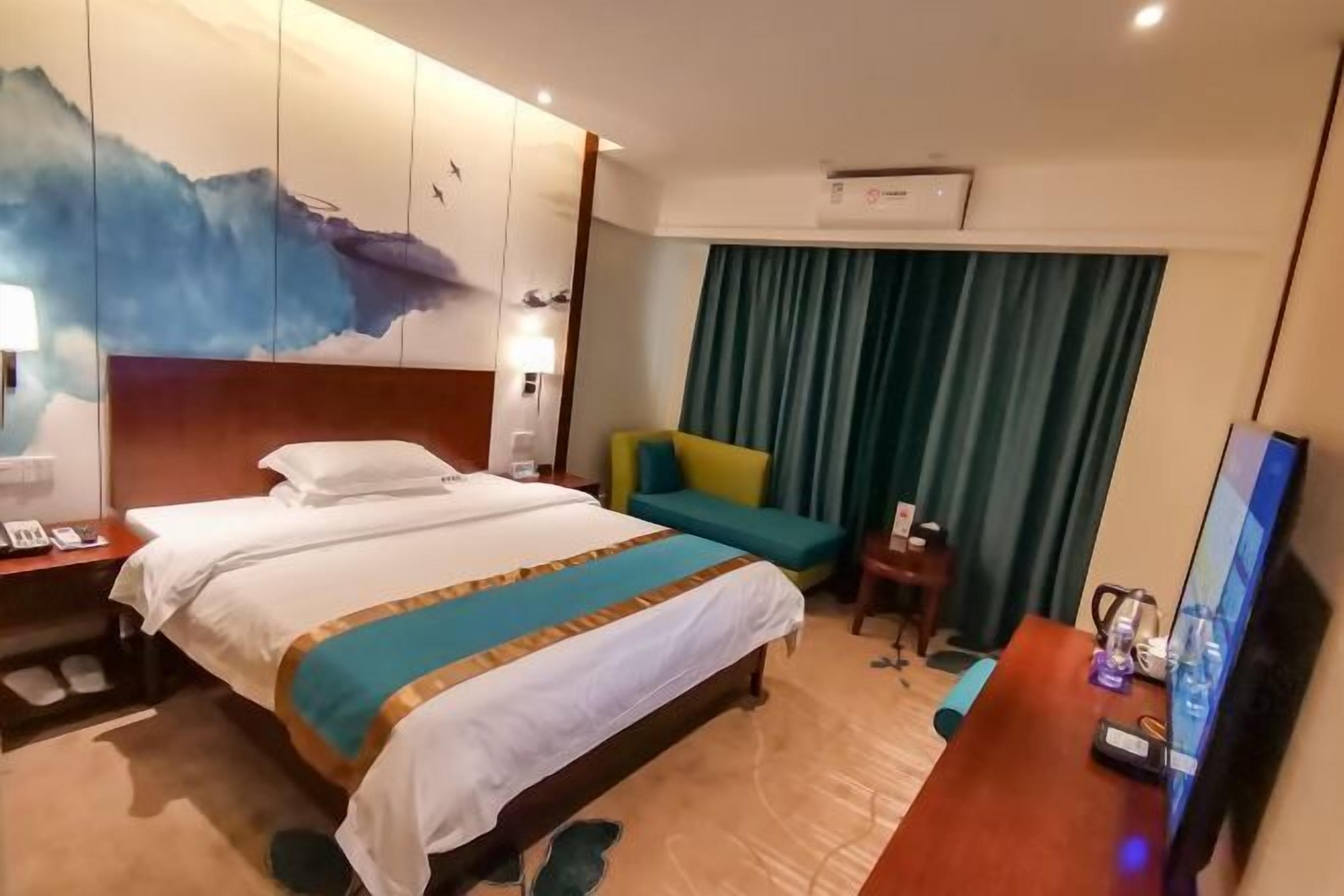 A hotel room with a bed, a desk, a TV, and a wall with a painting.