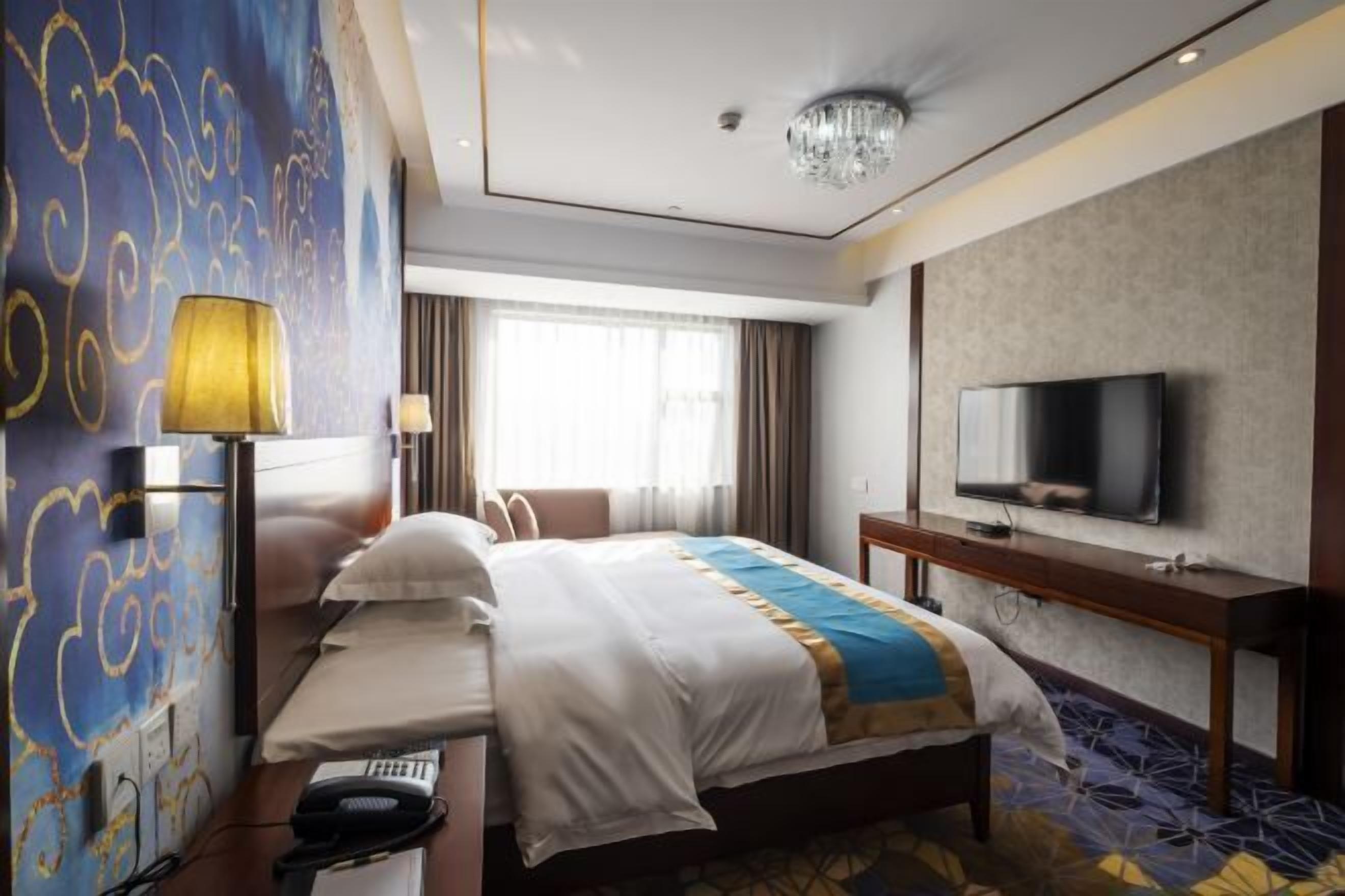 A hotel room with a large bed, a television, a desk, and a lamp.